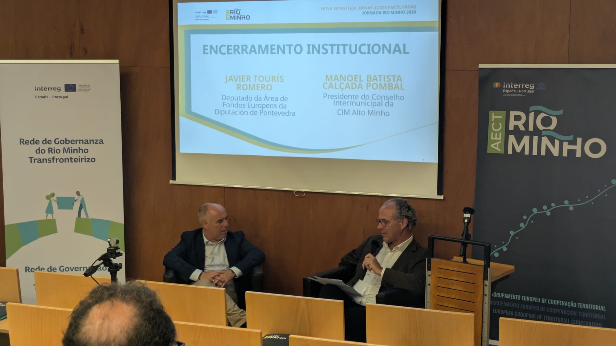 O presidente da CIM Alto Minho está sentado de frente para a plateia com um painel nas suas costas..