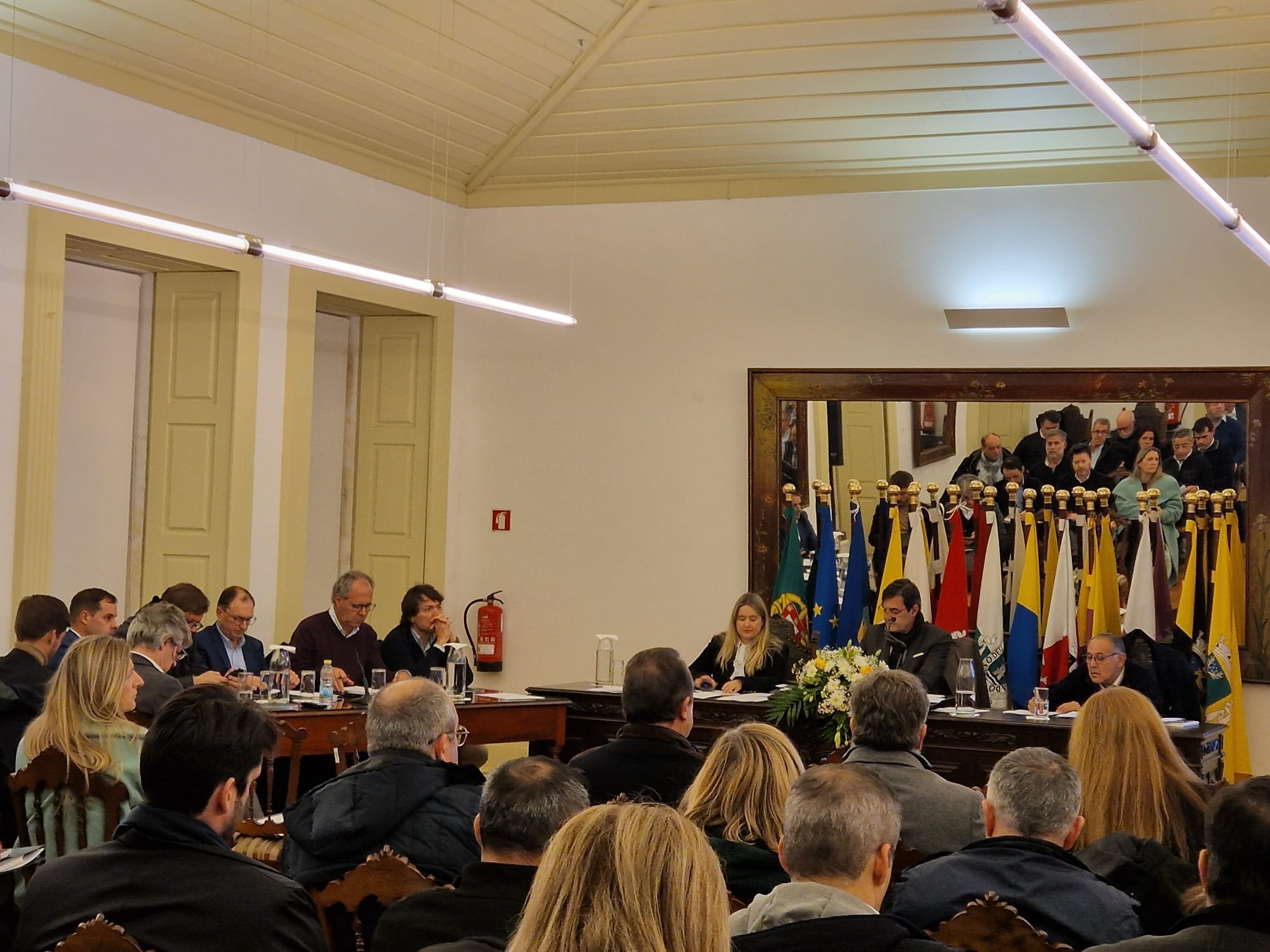 Na imagem vê-se a sala onde decorreu a reunião da Assembleia com os membros sentados de frente para uma mesa onde estão o Presidente da Assembleia e os secretários e de lado uma mesa onde estão sentados os Presidentes das câmaras municipais do alto Minho