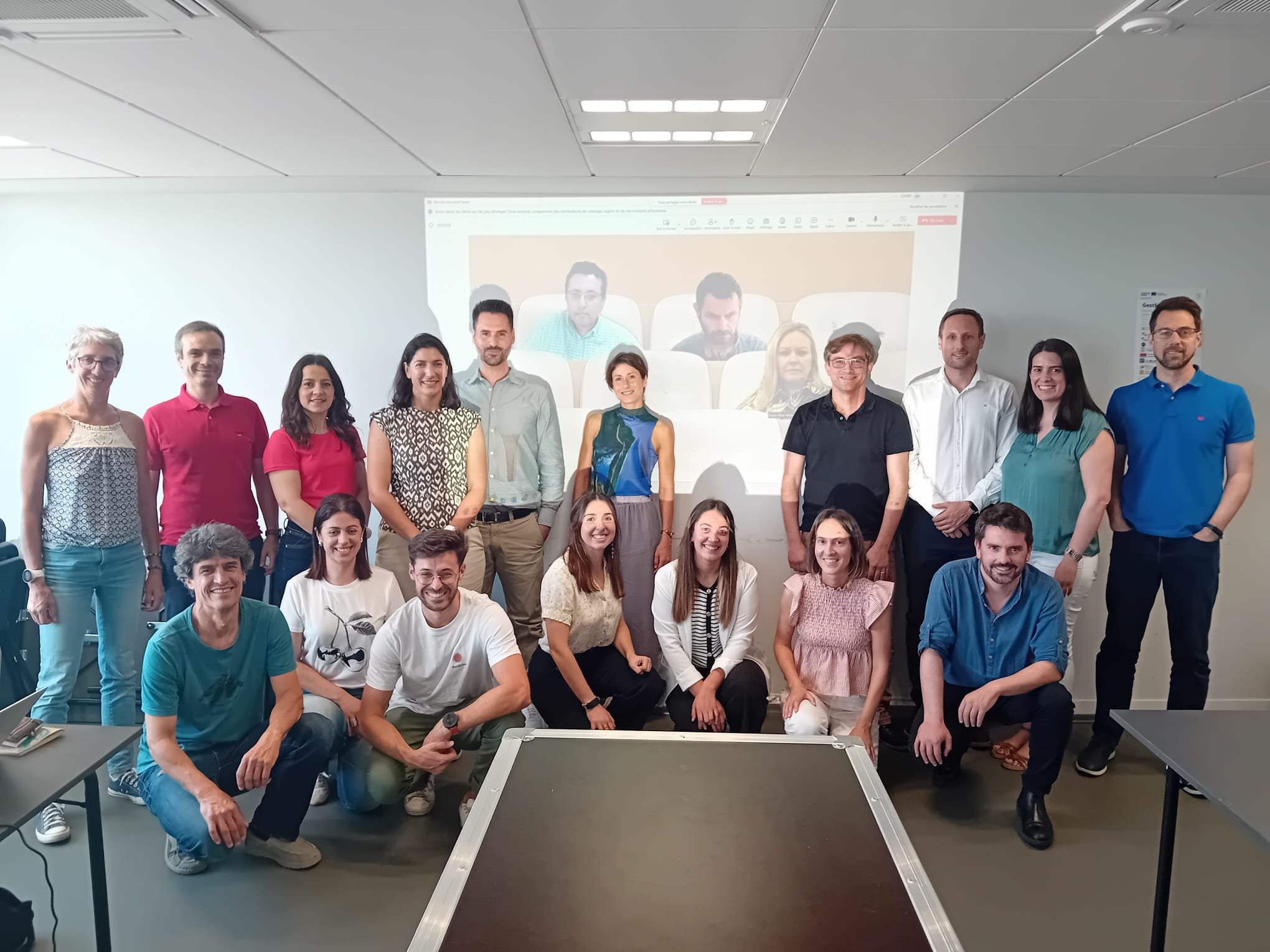 Os parceiros do projeto aparecem na imagem ao fundo e de pé, dispostos lado a lado, dentro de uma sala com uma tela de projeção por trás.