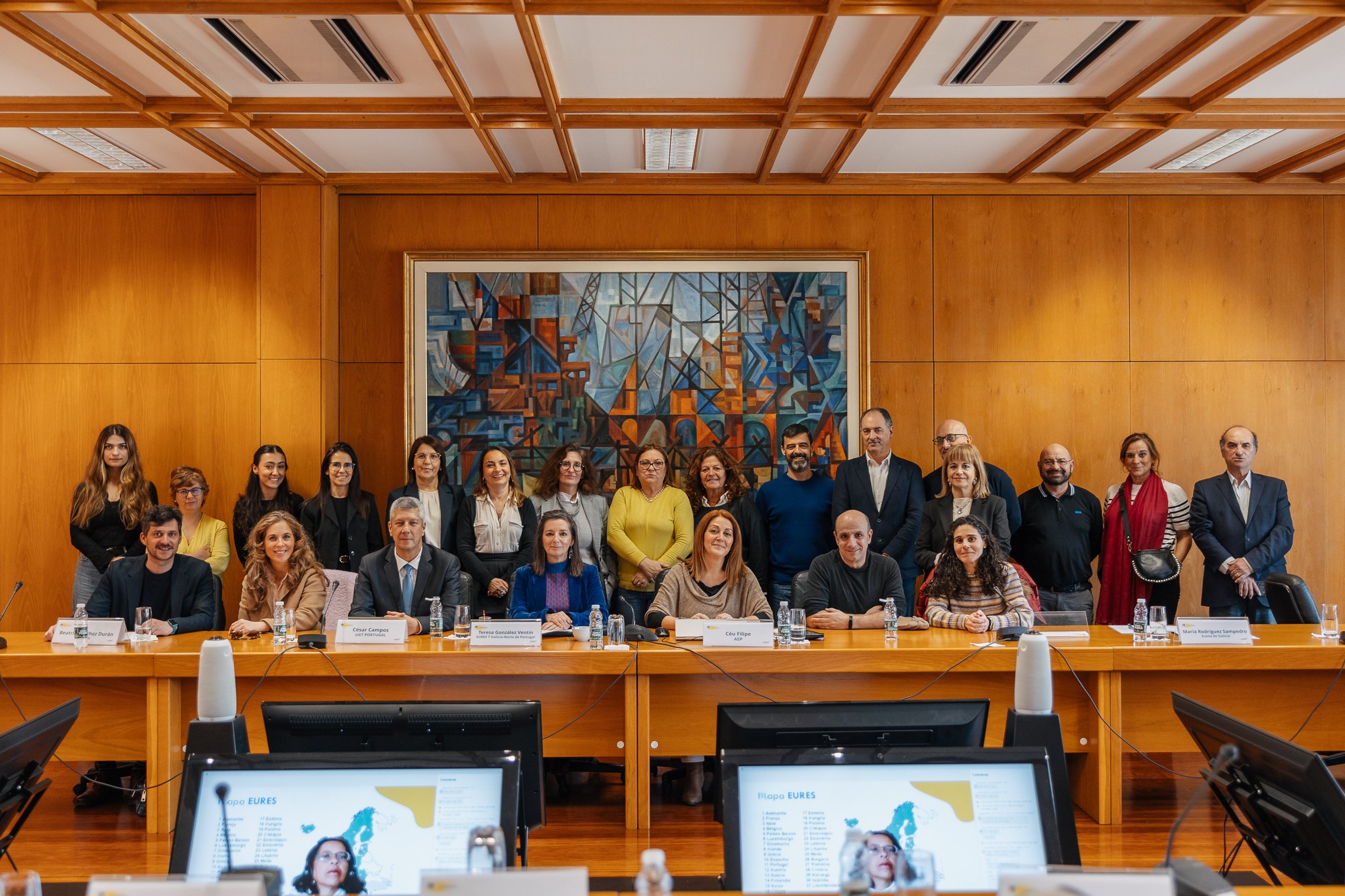 Participantes na reunião dispostos em duas filas. Na fila d ebaixo os participantes estão sentados e na segunda fila atrás, estão de pé.
