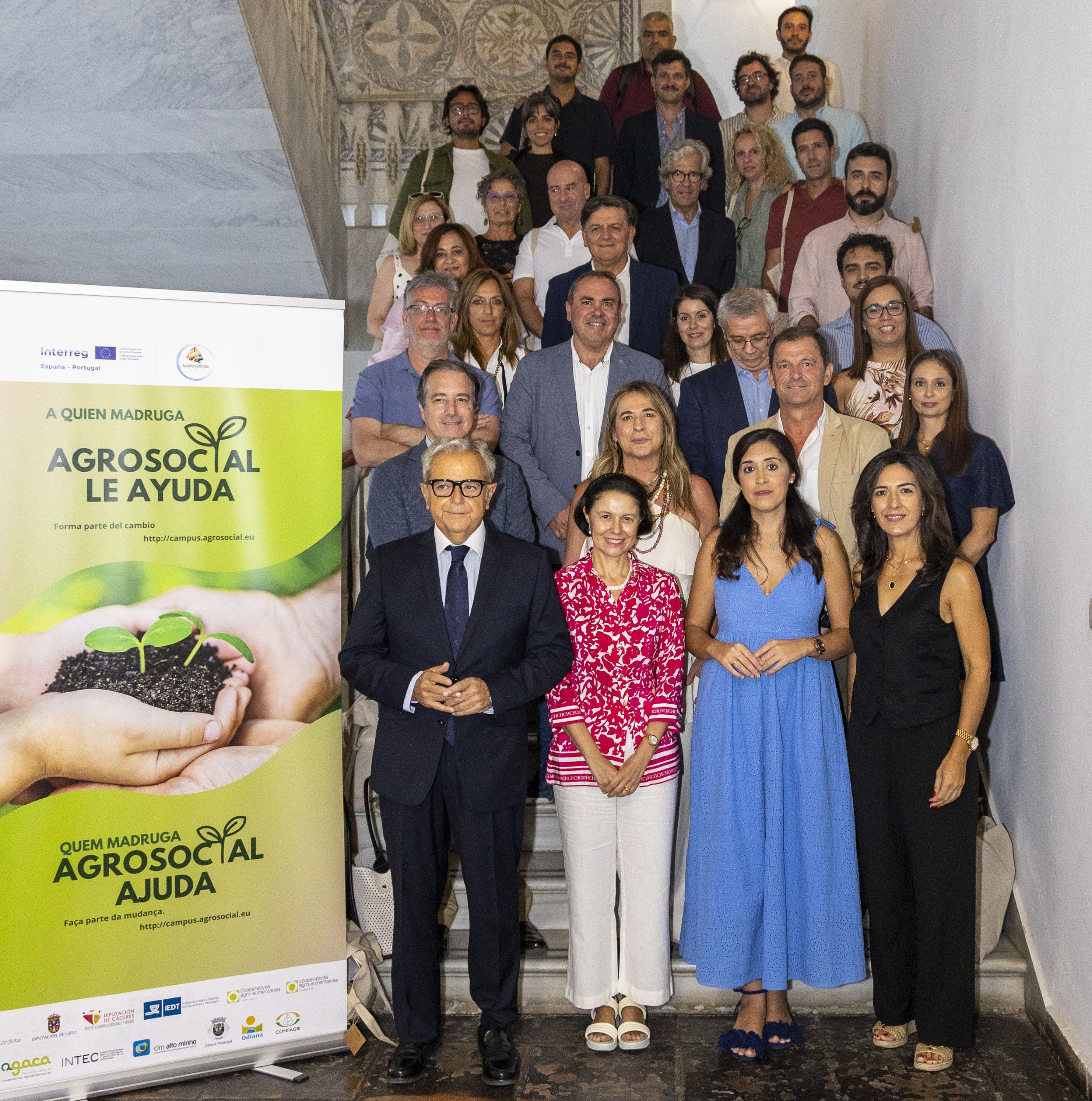 Fotografia de grupo, com cerca de 30 pessoas, reunidas numa escadaria. &Agrave; esquerda, v&ecirc;-se um painel do projeto AGROSOCIAL. O grupo est&aacute; sorridente e olha para a c&acirc;mara.
